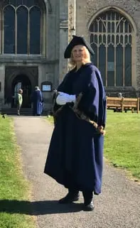 A person in dark ceremonial robes and a hat on the path outside a church.